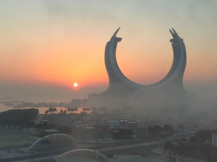 The Silver Pearl hotel in Doha is shrouded in fog with a rising sun behind.